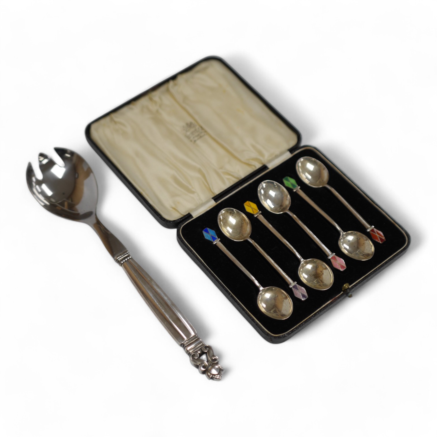 A 1980's Georg Jensen silver handled stainless steel Acorn pattern salad server, 23.8cm, together with a cased set of six Art Deco silver and polychrome enamel coffee spoons, W H Haseler Ltd, Birmingham, 1938. Condition